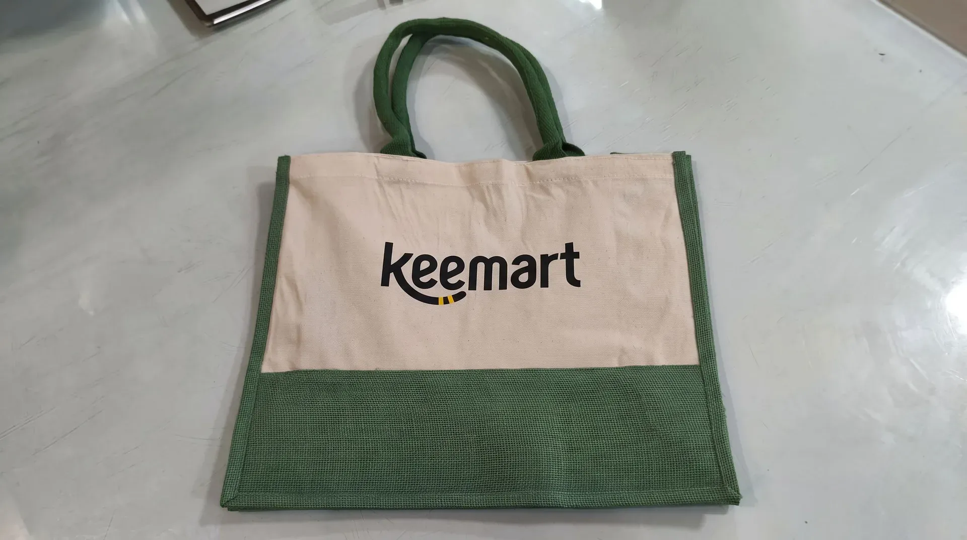 حقيبة توت صديقة للبيئة مصنوعة من الكتان الطبيعي والجوت الأخضر مع شعار Keemart الأسود الكبير على الواجهة.